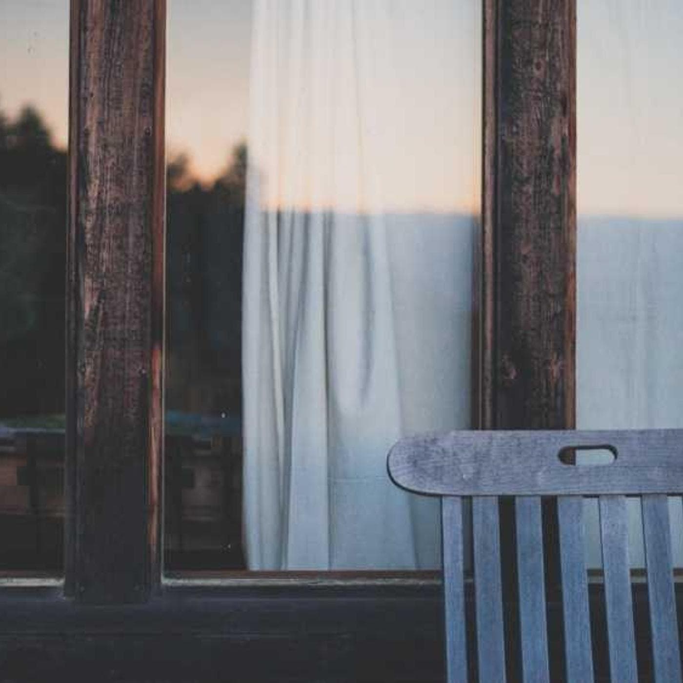 A single chair by a window with sheer curtains in the evening light
